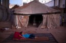 A refugee child lies on a matress in an abandoned factory near Syria's northern city of Aleppo on September 20, 2013