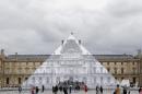 Tourists walk around theJR project at the Louvre Pyramid in Paris, Tuesday, May 24, 2016. For his latest bold project, street artist JR is creating an eye-tricking installation at the Louvre Museum that makes it seem as if the huge glass pyramid at the heart of the courtyard has disappeared. (AP Photo/Francois Mori)