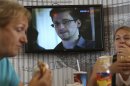 Transit passengers eat at a cafe with a TV screen with a news program showing a report on Edward Snowden, in the background, at Sheremetyevo airport in Moscow Wednesday, June 26, 2013. Russia's President Vladimir Putin said Tuesday that National Security Agency leaker Edward Snowden has remained in Sheremetyevo's transit zone, but media that descended on the airport in the search for him couldn't locate him there. (AP Photo/Sergei Grits)