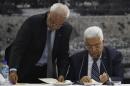 Palestinian chief negotiator Saeb Erekat helps Palestinian President Mahmoud Abbas as he signs international conventions during a meeting with Palestinian leadership in Ramallah