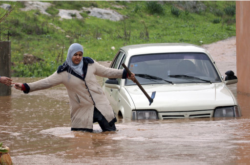 A Palestinian woman passes keys to a person on the other side of a flooded road in the West Bank of Jenin, Tuesday, Jan. 8, 2013. Stormy weather, including high winds and heavy rainfall, lashed Israel and the Palestinian territories, downing power-lines and trees. (AP Photo/Mohammed Ballas)