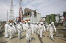 Members of the media and TEPCO employees, wearing protective suits and masks, walk in front of the No. 4 reactor building at the tsunami-crippled Fukushima Daiichi nuclear power plant in Fukushima prefecture