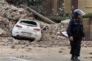 A Carabinieri paramilitary officer stands near a damaged car after a strong aftershock struck Finale Emilia