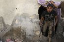 A Free Syrian Army fighter carrying his weapons walks out from a hole in a wall in Aleppo's Karm al-Jabal district
