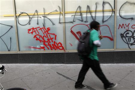A man walks past graffiti painted on a storefront in Oakland