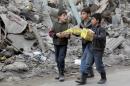 Boys carry boxes of biscuits near rubble of damaged buildings in Aleppo