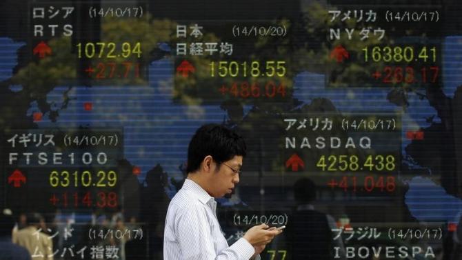 A pedestrian uses his mobile phone as he walks past an electronic board showing the stock market indices of various countries outside a brokerage in Tokyo