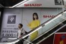 Man rides an escalator past Sharp Corp's advertisements at an electronics retail store in Tokyo