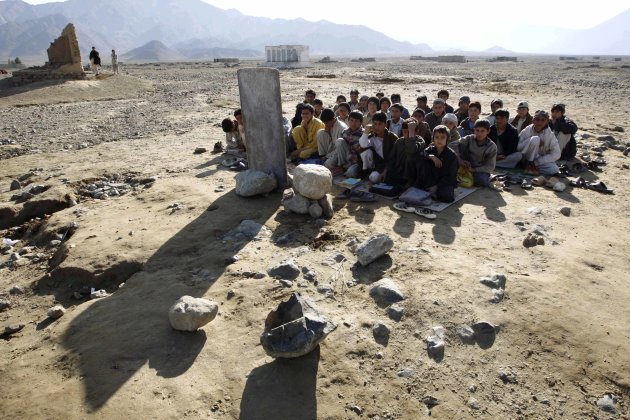 Afghan boys sit on the ground outdoors for their lesson near Khas Kunar refugee camp