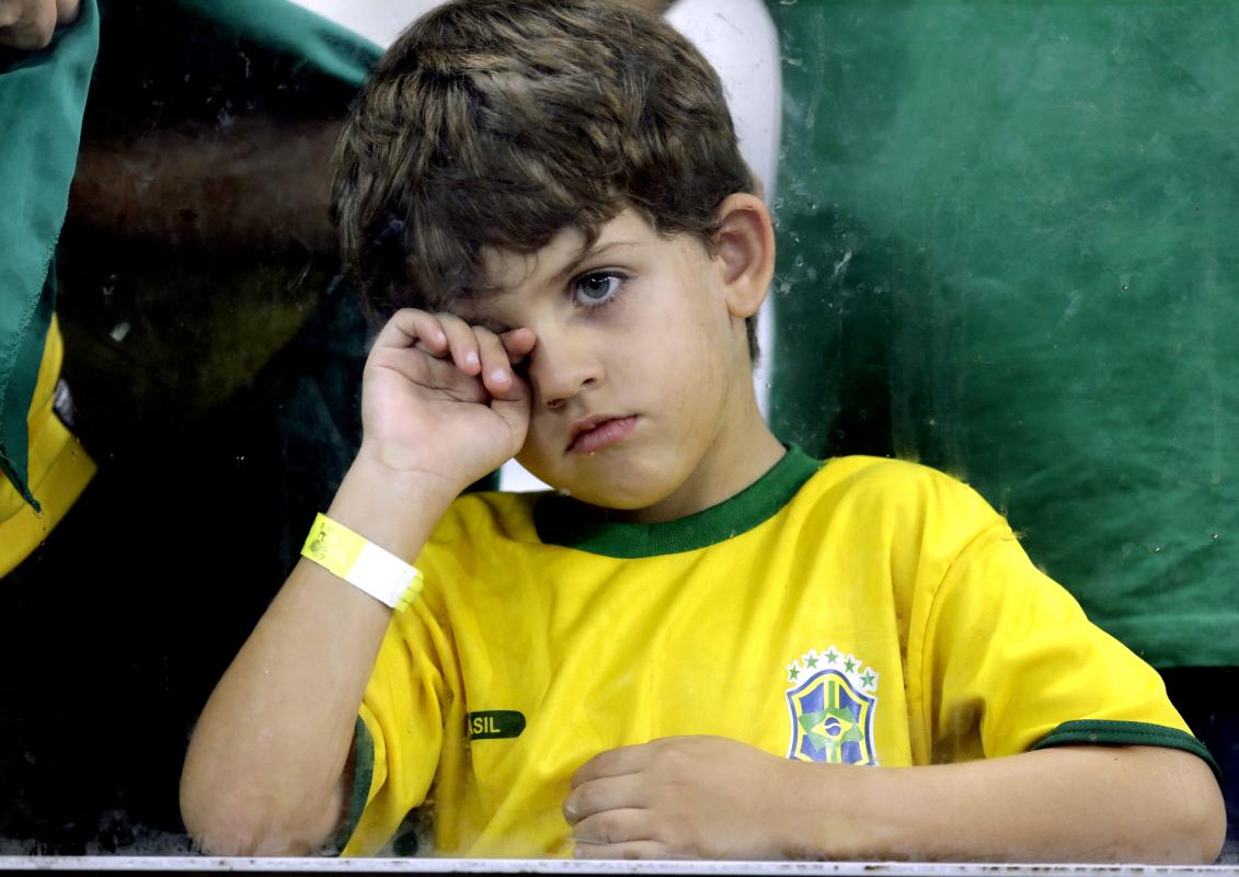 A young supporter watches players on the field after Germany defeated Brazil 7-1 to advance to the finals during the World Cup semifinal soccer match between Brazil and Germany at the Mineirao Stadium in Belo Horizonte, Brazil, Tuesday, July 8, 2014. (AP Photo/Natacha Pisarenko)