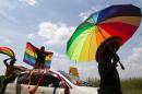 A person holds an umbrella bearing the colors of the rainbow as others wave flags during the the first gay pride rally since the overturning of a tough anti-homosexuality law, which authorities have appealed, in Entebbe, Uganda, August 9, 2014