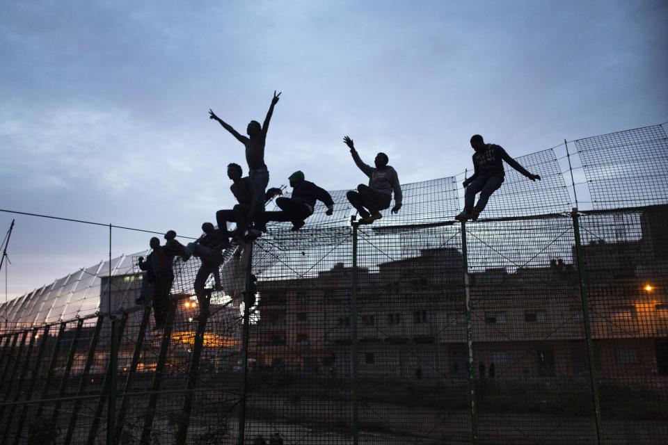 FILE - In this Friday, March 28, 2014, file photo, Sub-Saharan migrants climb over a metallic fence that divides Morocco and the Spanish enclave of...