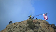 This Sunday, July 1, 2012 video image taken from AP video shows a group of firefighters raising an American flag above a section of the burned out neighborhood, Mountain Shadows, Colo. Almost 350 homes burned to the ground last week in the Waldo Canyon fire, one of many still raging across the West. (AP Photo/AP Video, C.J. Moore)