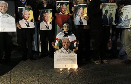 Palestinians light candles and hold placards bearing images of former South African President Nelson Mandela outside the Church of Nativity in the West Bank town of Bethlehem