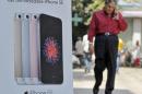 A man speaks on his mobile phone as he walks past an Apple iPhone SE advertisement billboard in a street in New Delhi